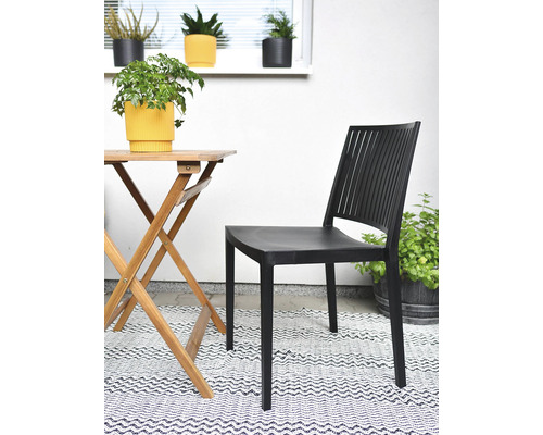 Scéna s černou plastovou zahradní židlí, dřevěným stolem a dekorací venku.