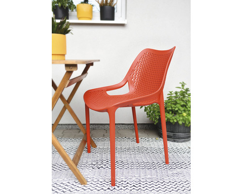 Oranžová plastová židle s područkami vedle dřevěného stolu na terase