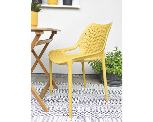 Žlutá plastová židle s područkami vedle dřevěného stolu na balkoně