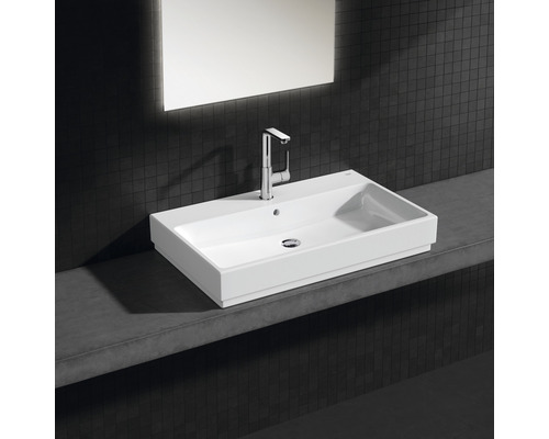 Obdélníkové keramické umyvadlo s baterií na poličce v koupelně.