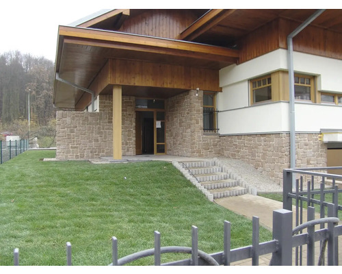 Vnější pohled na budovu s kamennou fasádou, dřevěnými prvky a trávníkem