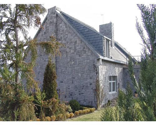 Fasáda domu z přírodního kamene se střechou z tašek obklopená zahradními prvky.