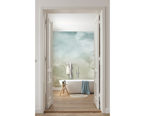 Světlá koupelna s vanou, stoličkou a tapetou se vzorem oblaků, pohled skrz otevřené dveře.