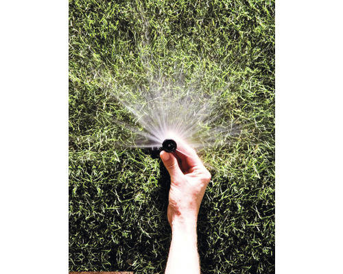 Ruka drží zavlažovač trávníku, který stříká vodu.