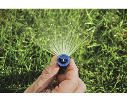 Ruka drží zavlažovač trávníku, který stříká vodu