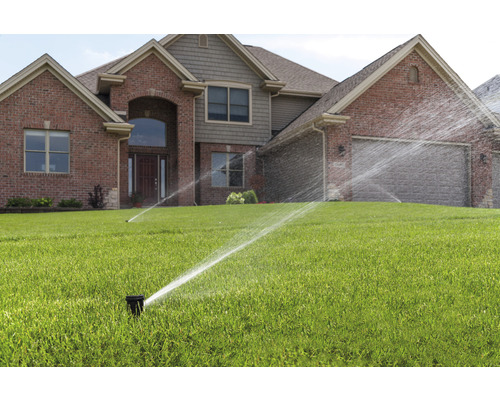 Zavlažovací systém s trávníkovými postřikovači před domem.