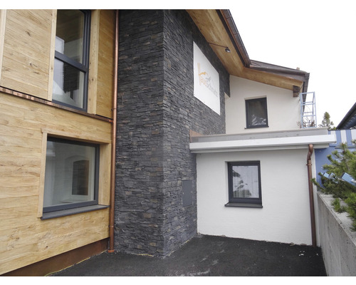 Venkovní pohled na dům s dřevěnou fasádou, zdí z přírodního kamene a okapem