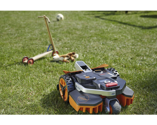 Robotická sekačka na trávníku s hračkami v pozadí