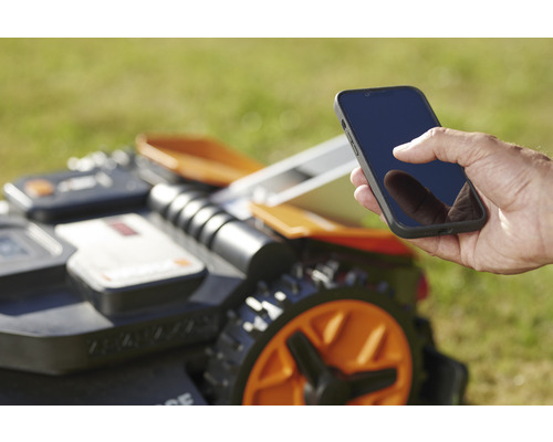 Muž ovládá robotickou sekačku pomocí smartphonu.