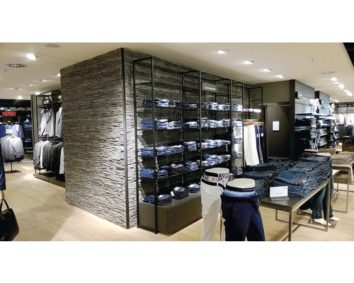 Interiérová fotografie obchodu s oblečením s regály plnými džínů a jiných oděvů