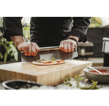 Osoba krájí pizzu škrabkou na těsto na dřevěném prkénku.