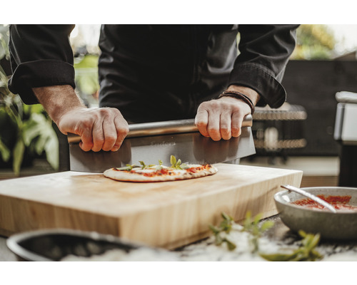 Osoba krájí pizzu škrabkou na těsto na dřevěném prkénku.