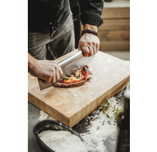 Osoba krájí pizzu na dřevěném prkénku pomocí kráječe na pizzu.