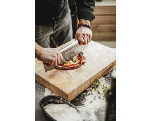 Osoba krájí pizzu na dřevěném prkénku pomocí kráječe na pizzu.