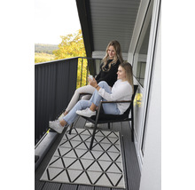 Dvě ženy sedí na balkóně s geometrickým kobercem a výhledem na krajinu.
