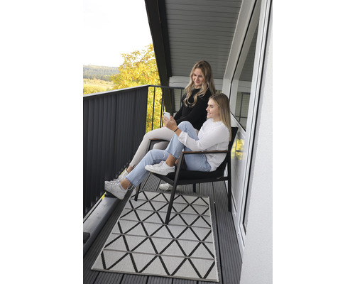 Dvě ženy sedí na balkóně s geometrickým kobercem a výhledem na krajinu.