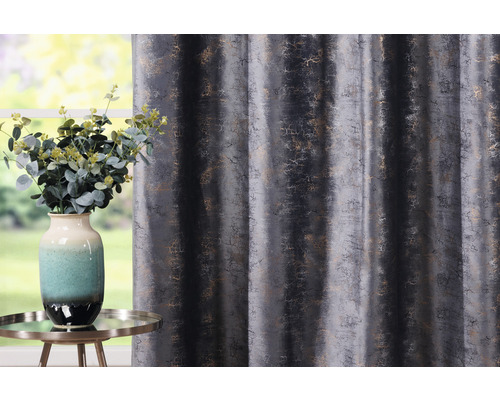 Dekorativní závěs s abstraktním vzorem vedle vázy s květinami na stole.