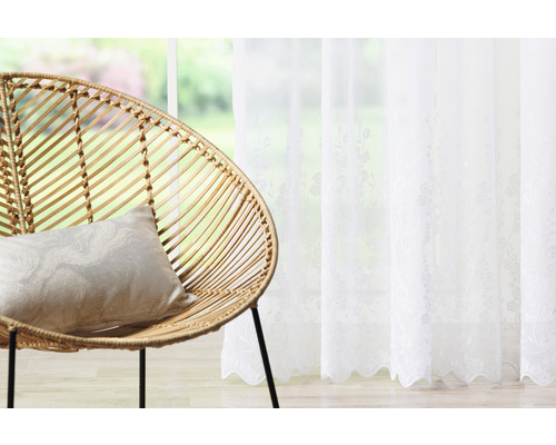 Dekorativní obytné prostředí s ratanovým křeslem, polštářem a bílým závěsem s květinovým vzorem
