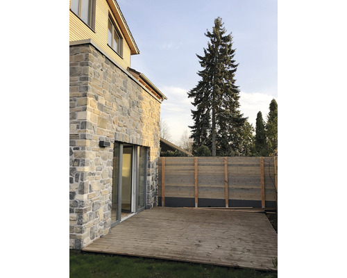 Dům s fasádou z přírodního kamene, dřevěnou terasou a dřevěným plotem v zahradě.