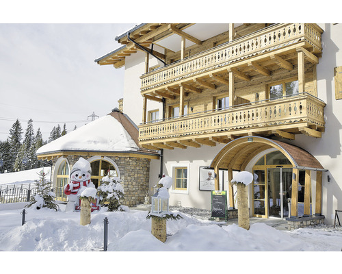 Exteriér domu s dřevěnými balkony v zimě a figurkou sněhuláka.