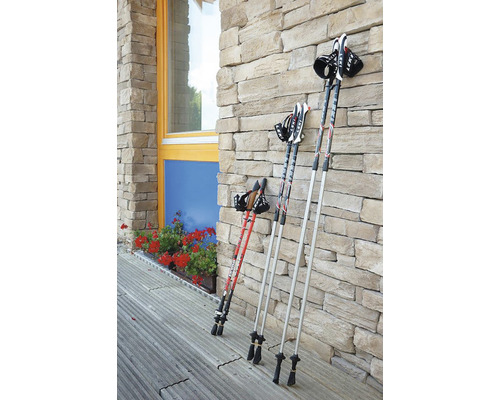 Několik trekových holí opřených o kamennou zeď.