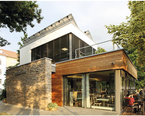 Vnější pohled na moderní budovu s kamennou zdí, dřevěným obkladem a solárním systémem na střeše.