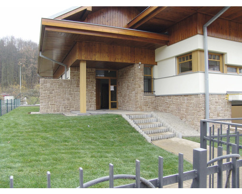 Vnější pohled na budovu s kamennou zdí, dřevěnou střechou a trávníkem