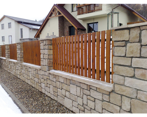 Plot je ohraničen kamennou zdí a dřevěnými plotovými latěmi.