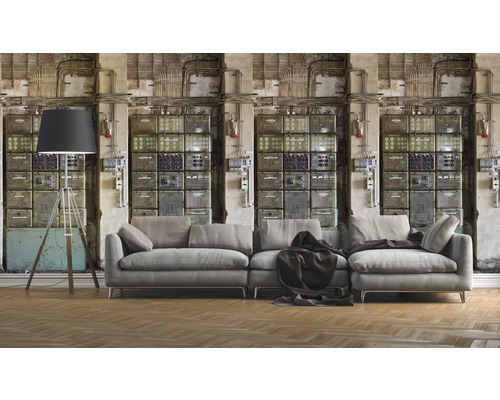 Obývací pokoj s šedou pohovkou, stojací lampou a nástěnnou tapetou s motivem rozvaděče pro industriální atmosféru.