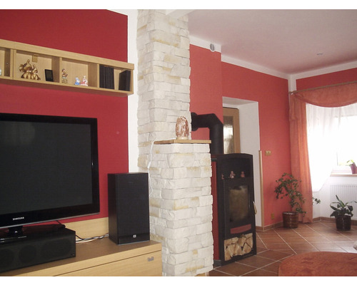 Obývací pokoj s kamny, zděným sloupem, televizí a dřevěnou policí