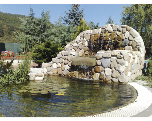 Zahradní jezírko s vodopádem z kamenů v zelené zahradě.