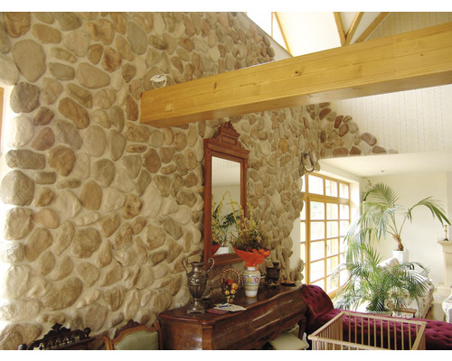 Interiér pokoje s kamennou zdí, dřevěnými trámy a různým nábytkem.