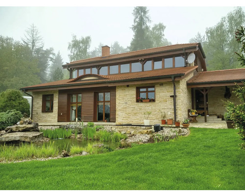 Dům s kamennou zdí, dřevěnými okny a jezírkem v zahradě.