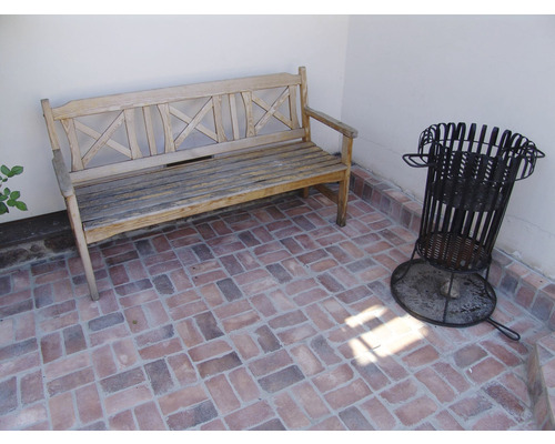 Zahradní scéna s dřevěnou lavicí a ohništěm na dlážděné ploše.