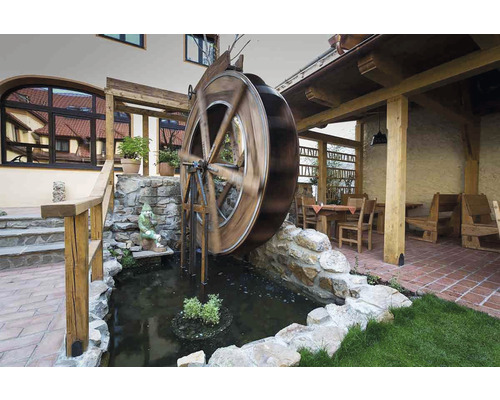 Scéna s vodním kolem, které se otáčí v rybníku, obklopené kameny a zelení