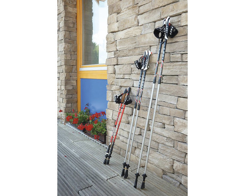 Tři páry trekingových holí z kovu opřené o kamennou zeď.