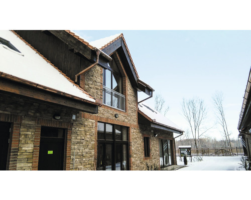 Vnější pohled na dům s kamennou zdí a zasněženou střechou.