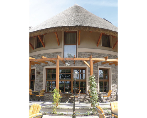 Kulatý dům se slámovou střechou, kamennou fasádou a dřevěnými okny a venkovním posezením se stoly a židlemi