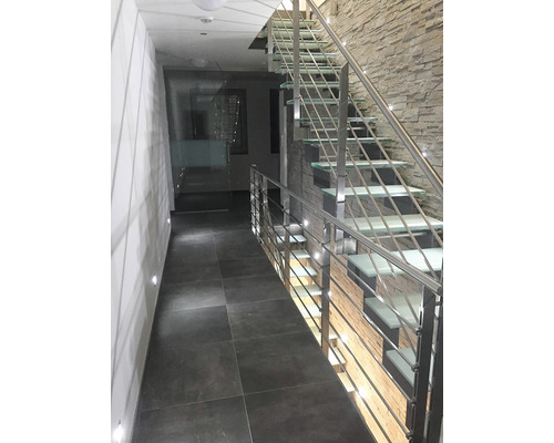 Interiérový snímek chodby se schodištěm, dlažbou a kamennou stěnou