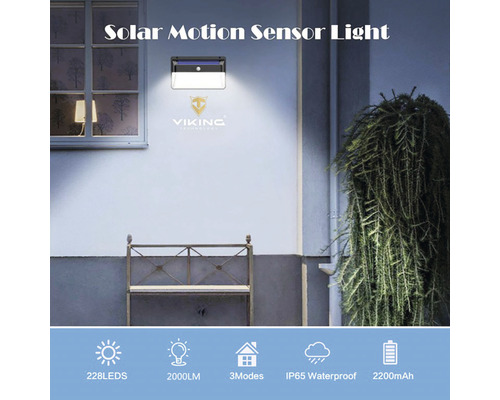 Solární světlo se snímačem pohybu na stěně domu, osvětluje lavičku a rostlinu.