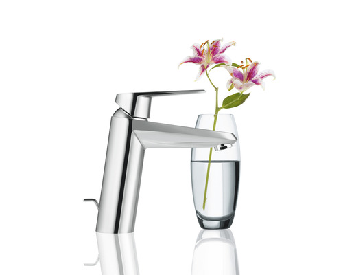 Moderní kovová vodovodní baterie vedle vázy s květinami