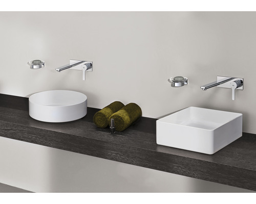 Koupelna s kulatými a obdélníkovými umyvadly na desku, bateriemi a ručníky na tmavé polici