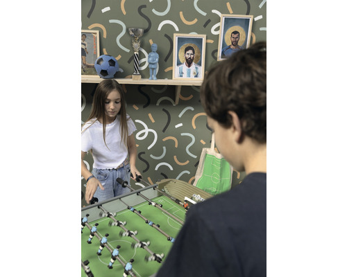 Dvě děti hrají stolní fotbal v místnosti se zdí s grafickým vzorem