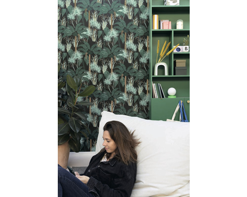 Obývací pokoj s tapetou s motivem džungle, zelenými regály a ženou sedící na sedacím vaku