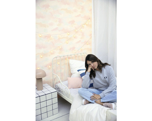 Světlá ložnice s kovovou postelí, světelným řetězem a mladou ženou