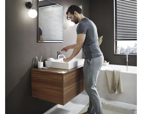 Moderní koupelna s umyvadlem, skříňkou, zrcadlem a mužem myjícím si ruce