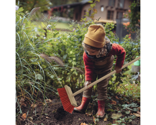 Dítě zametá listí na zahradě koštětem.