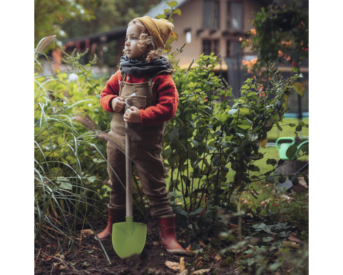 Dítě s lopatou stojí na zahradě.