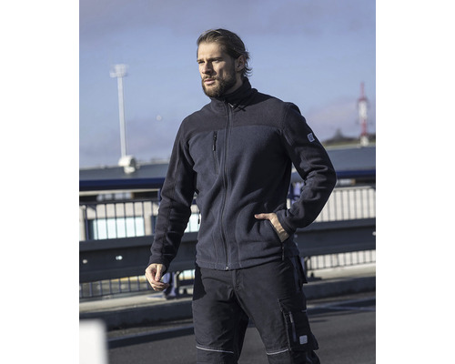 Muž má na sobě pracovní oděv: fleecovou bundu a pracovní kalhoty