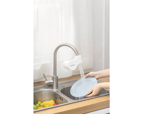 Scéna kuchyňského dřezu s vodovodním filtrem a osobou myjící talíř